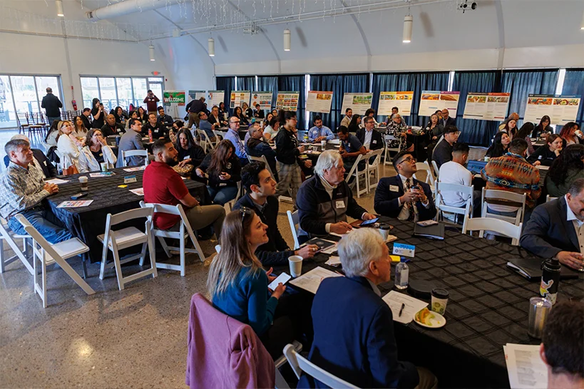 Large meeting of people sitting at round tables.