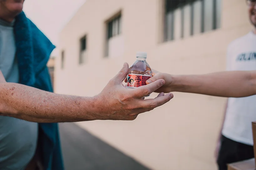 A man handing a water bottle to another person.